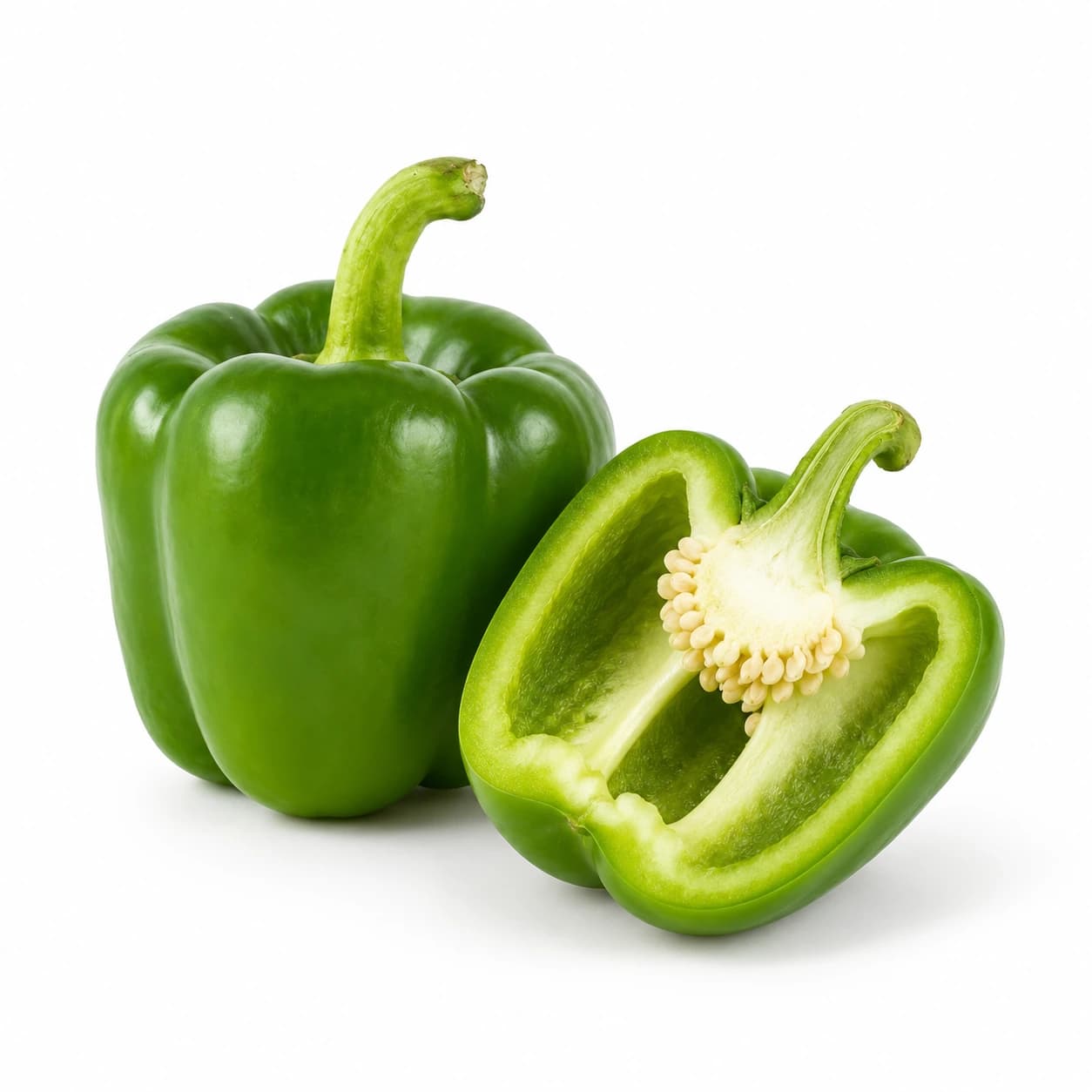 Cela zelena paprika in prerezana polovica s svetlimi notranjimi rebri ter semeni.
